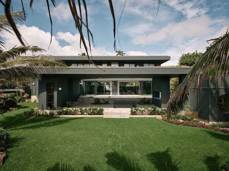 Garden approach across lawn framed by swaying palm fronds under a partly cloudy sky