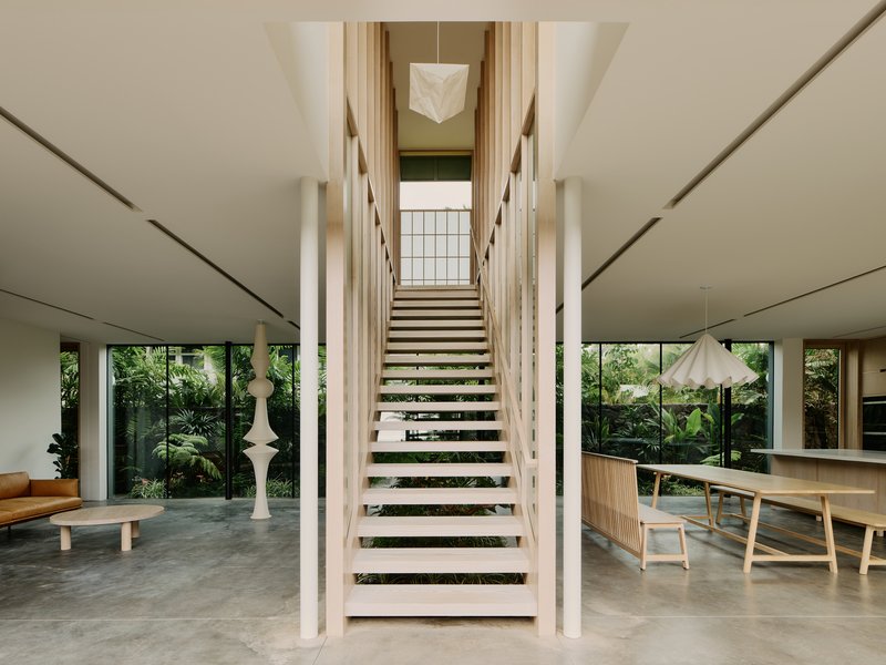 Central open-tread timber staircase flanked by white sculptural columns in the double-height living space