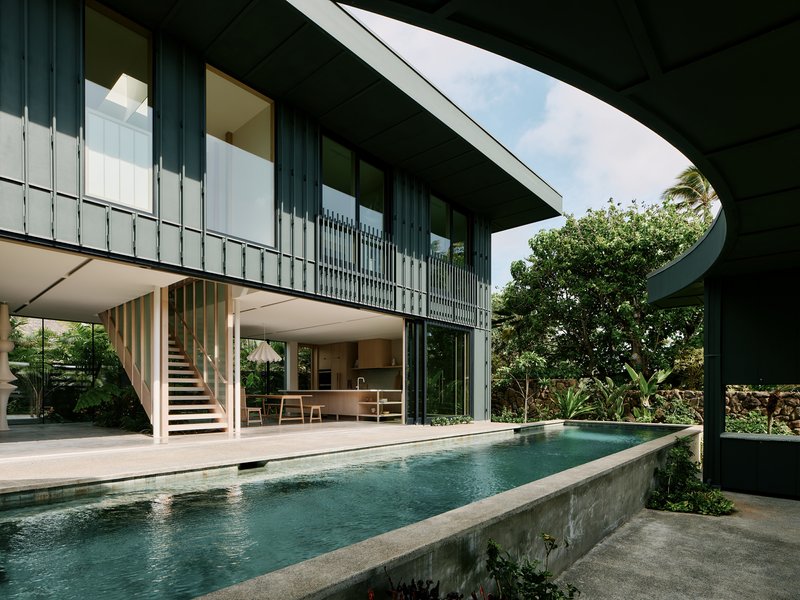 Elevated lap pool with concrete walls beside an open-plan living area and timber stair under a curved roof