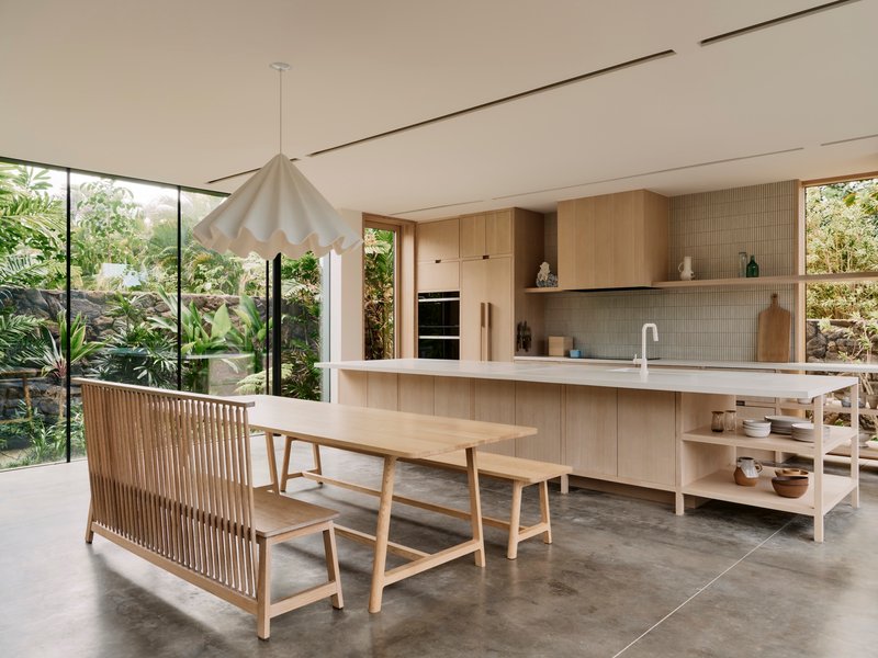 Kitchen island with timber bench seating and pendant light beside floor-to-ceiling glazing overlooking garden