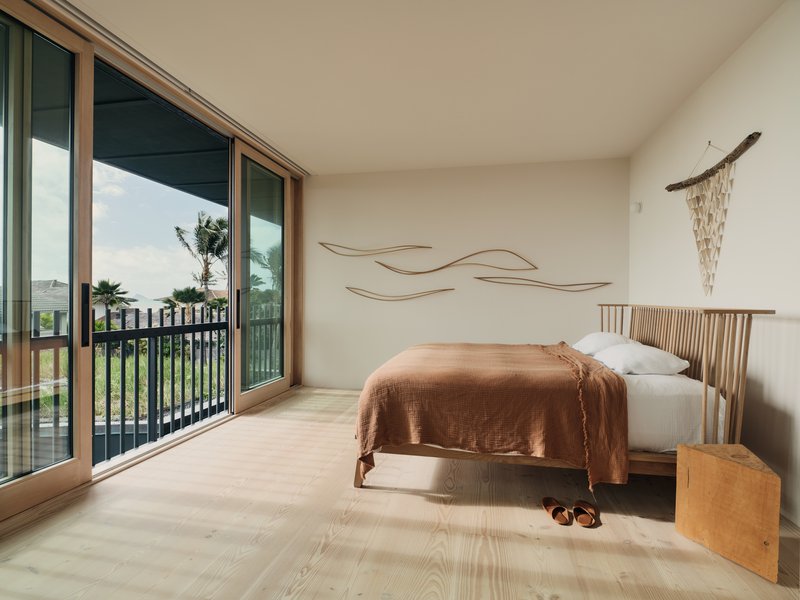 Bedroom with timber-framed sliding glass doors opening onto a balcony overlooking palm trees