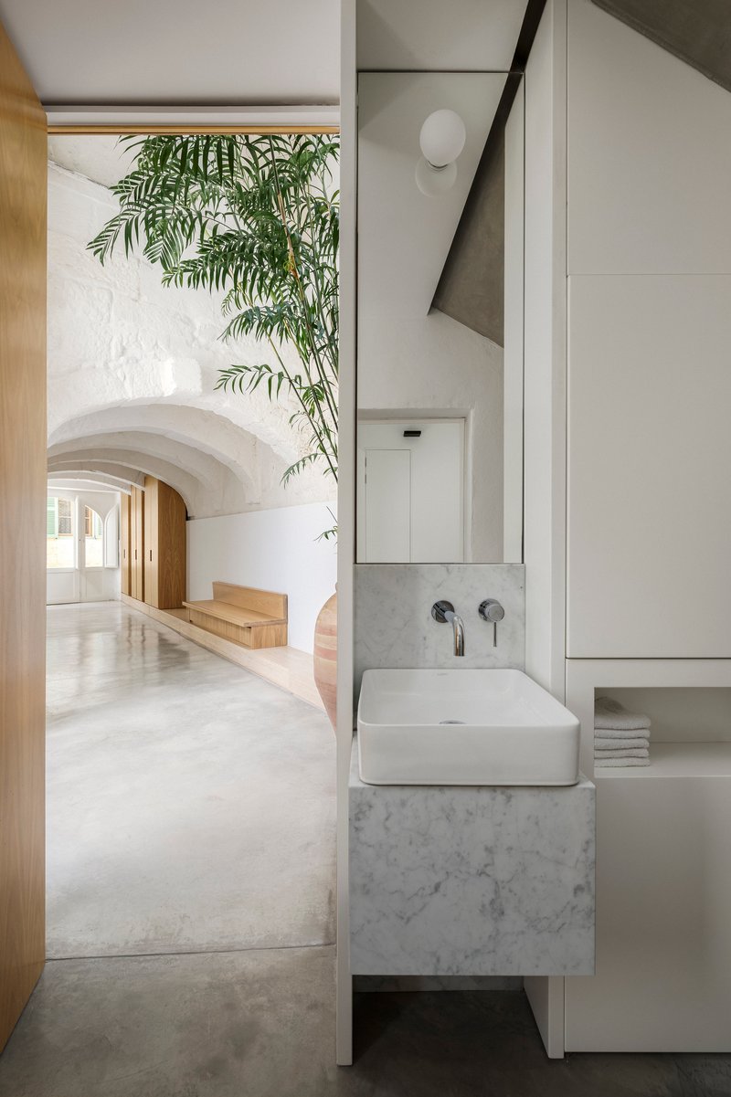 Bathroom with floating marble sink beneath an arched corridor and overhanging palm fronds