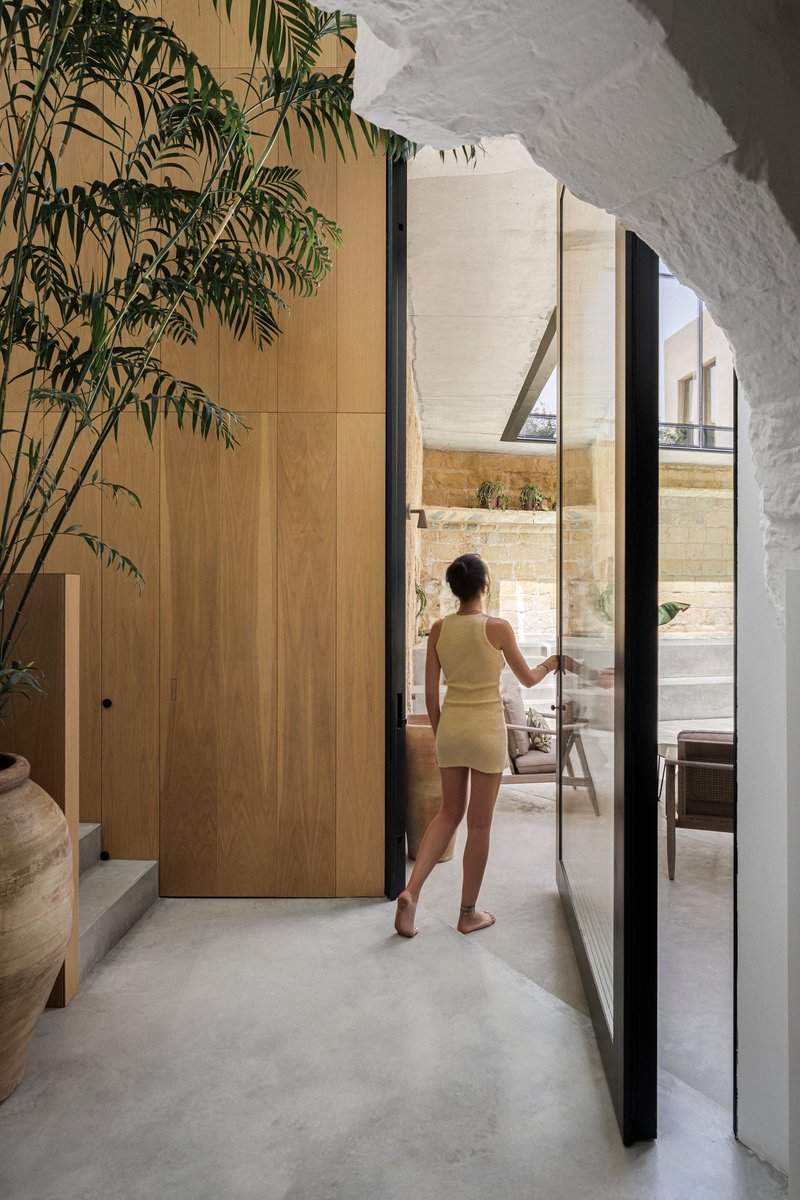 Woman opening glass door to courtyard from timber-clad hallway with potted palm