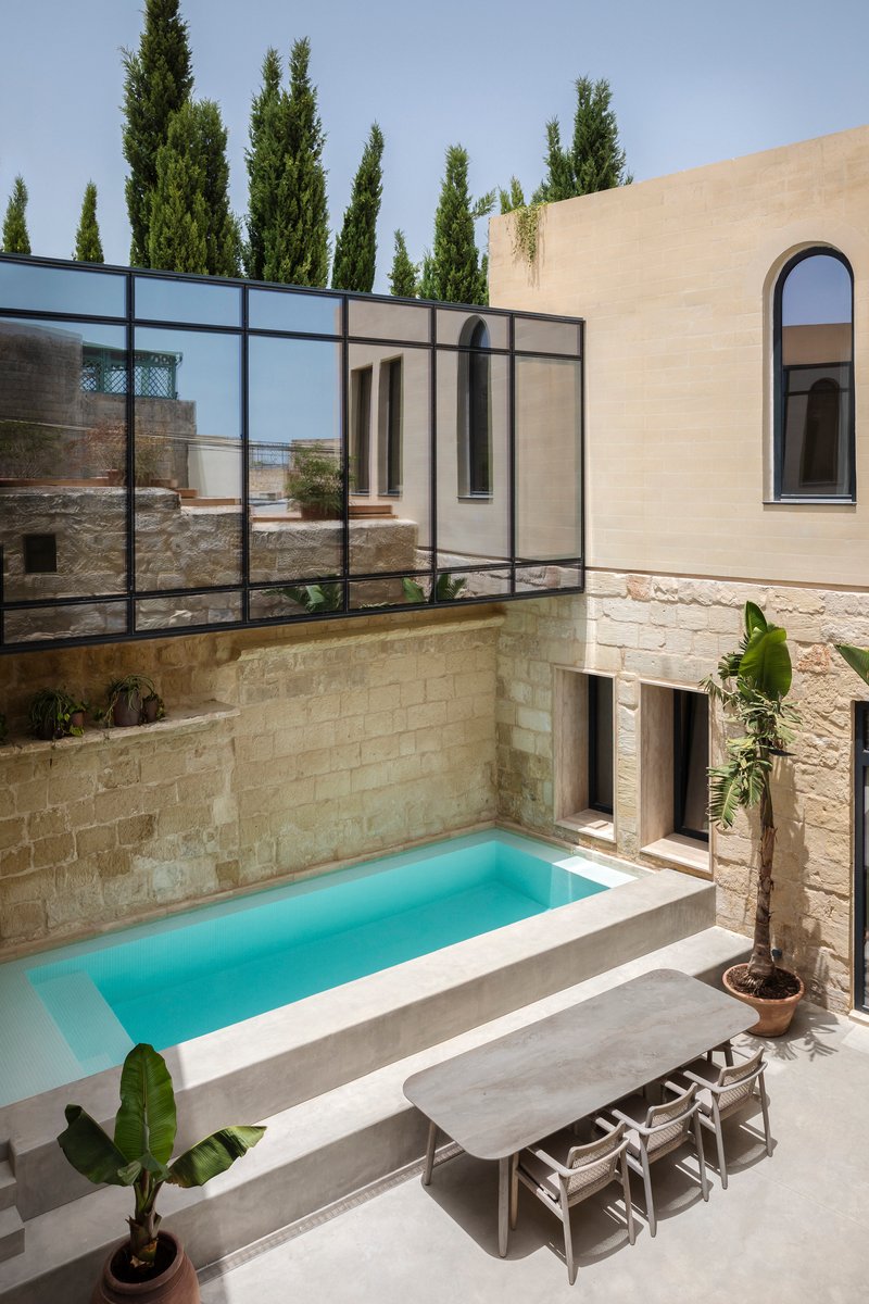 Courtyard pool surrounded by stone walls and black steel glazing with cypresses beyond
