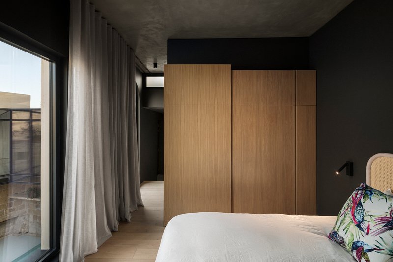 Bedroom with oak wardrobe panels, grey curtains and exposed concrete ceiling