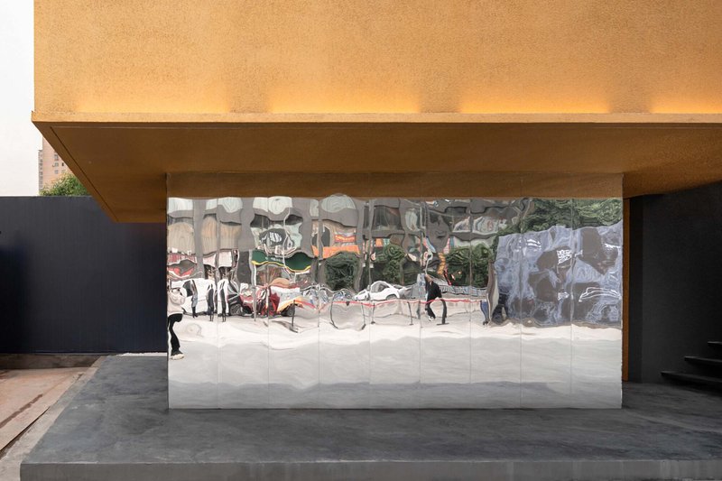 Covered entrance with reflective mirrored wall beneath a cantilevered overhang and pedestrian visible in reflection