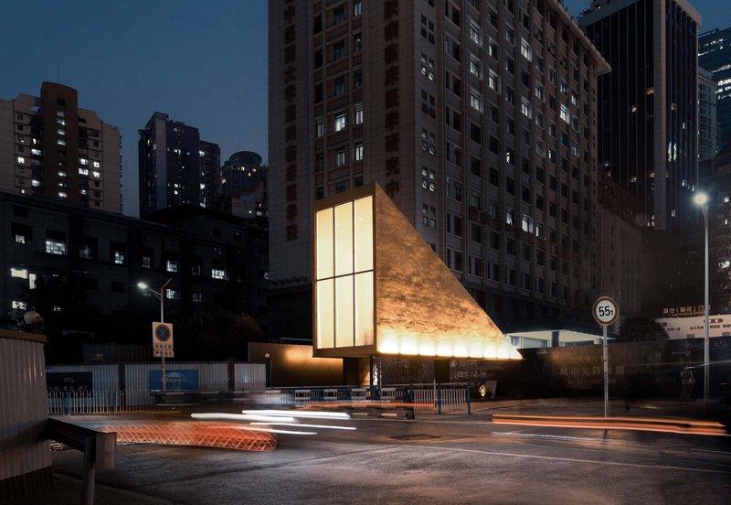 Two-story pavilion with glass windows and angled metal cladding framed by light trails at dusk
