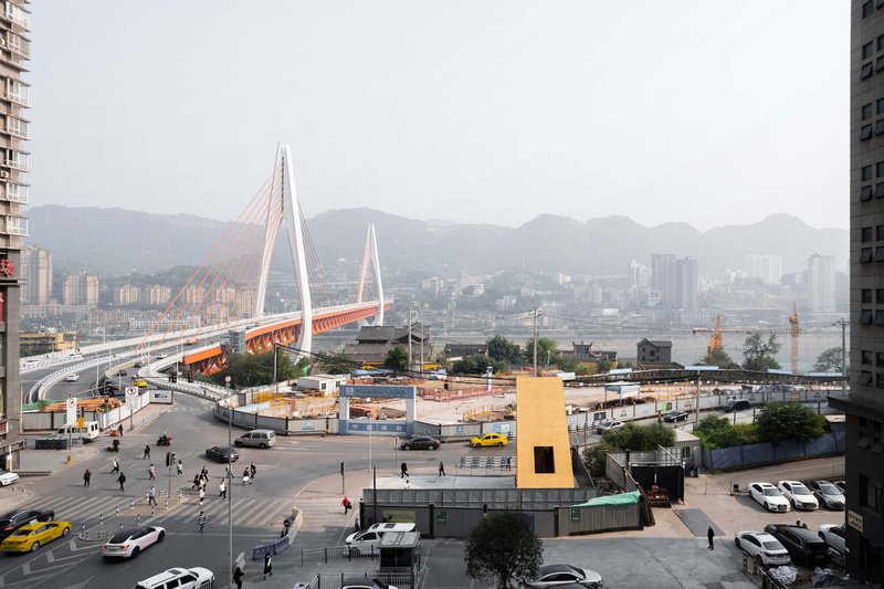 Yellow kiosk structure in foreground with cable-stayed bridge and mountains visible beyond