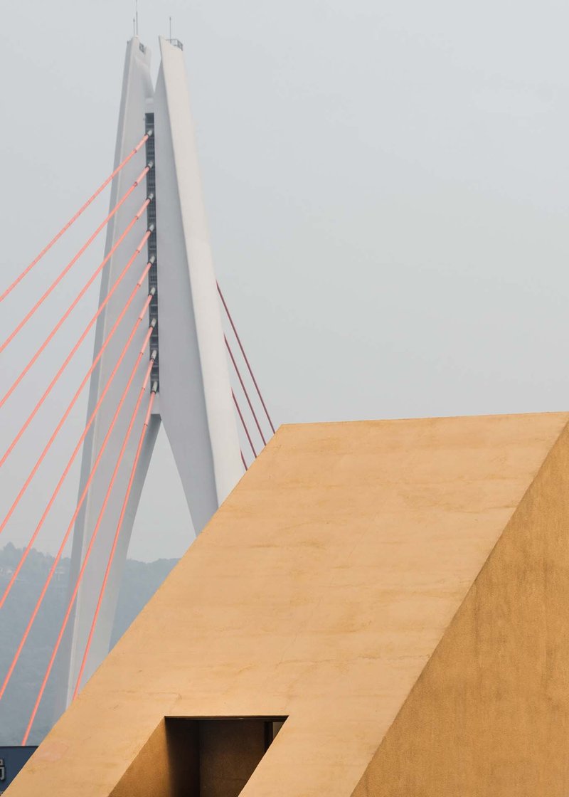 Angular ochre volume with rectangular aperture against the white pylon of a cable-stayed bridge