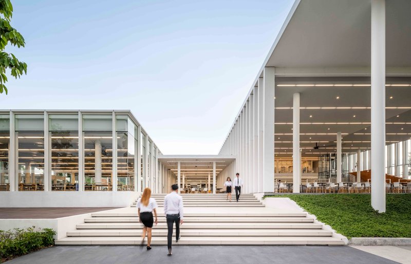 Wide stepped entry plaza with two figures ascending toward the recessed glazed volumes