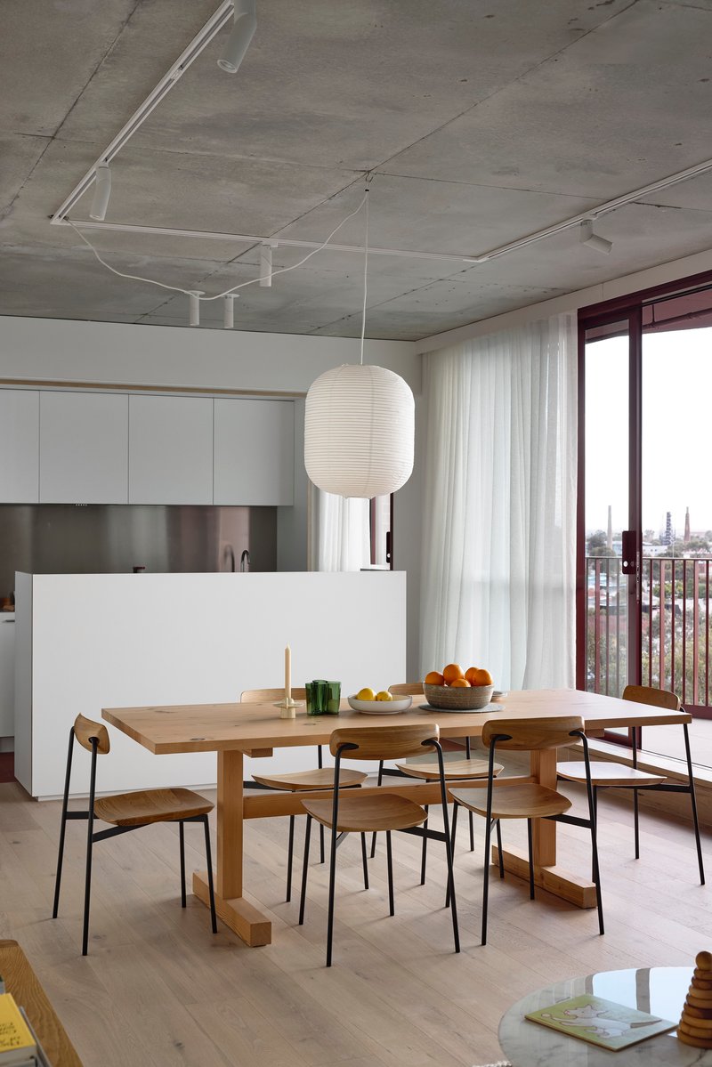 Open kitchen and dining area with exposed concrete ceiling and sheer curtains at the balcony door