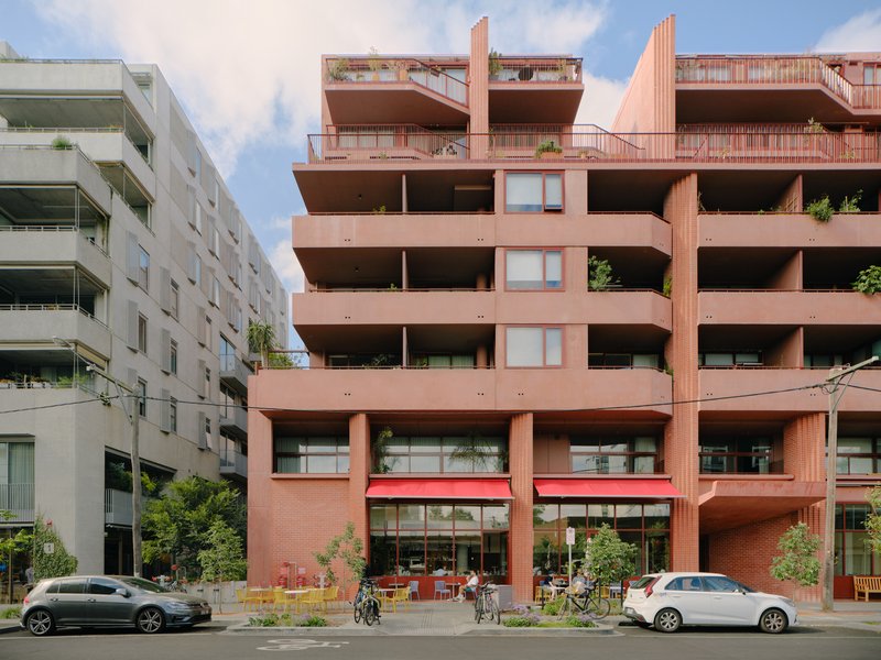 Street view of the terracotta brick facade with deep recessed balconies and ground floor cafe