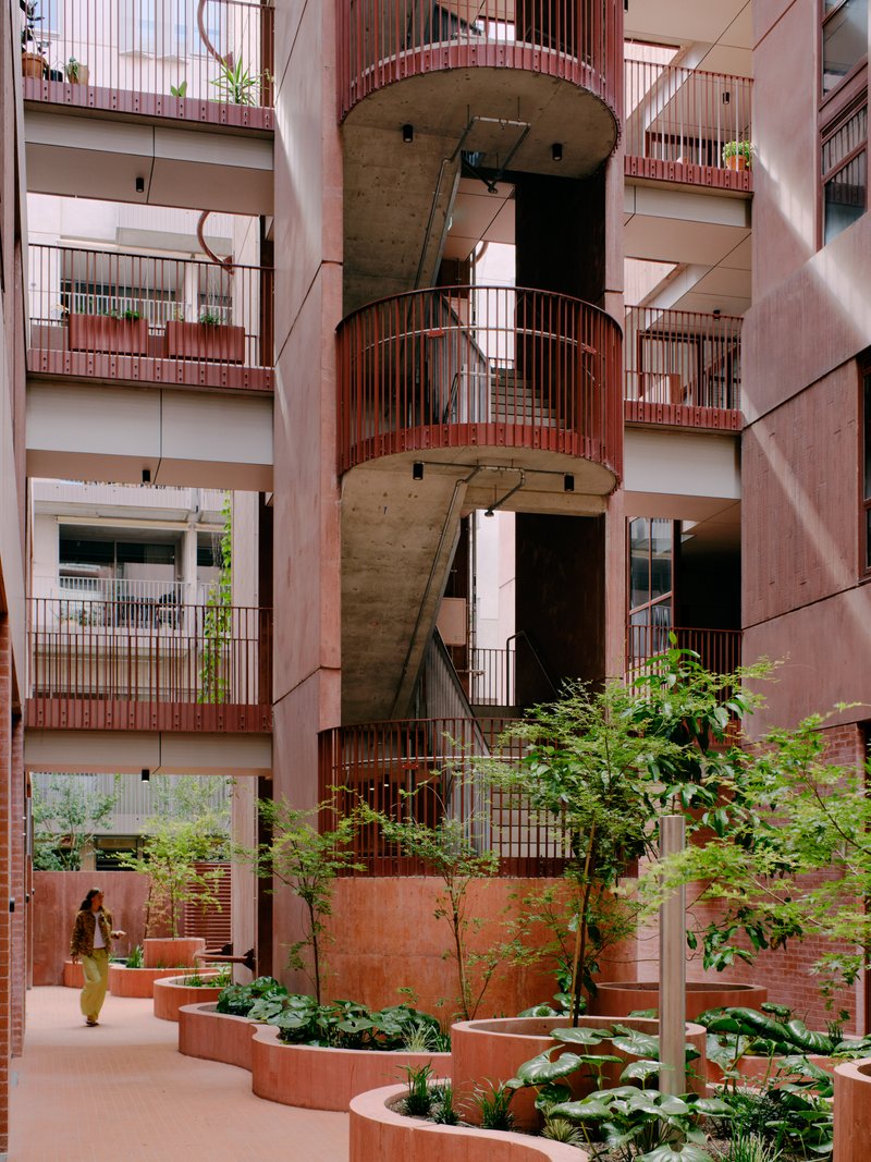 Central courtyard with concrete spiral stair wrapped by pink metal railings and planted beds below