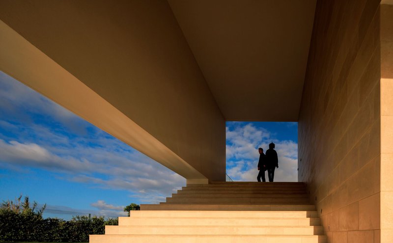 Stone staircase framing two figures silhouetted against blue sky with scattered clouds