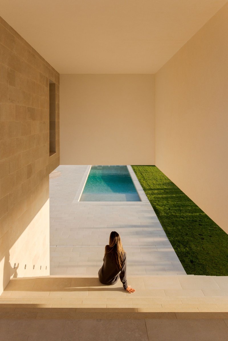 Courtyard with rectangular pool bordered by white paving and grass strip with seated figure