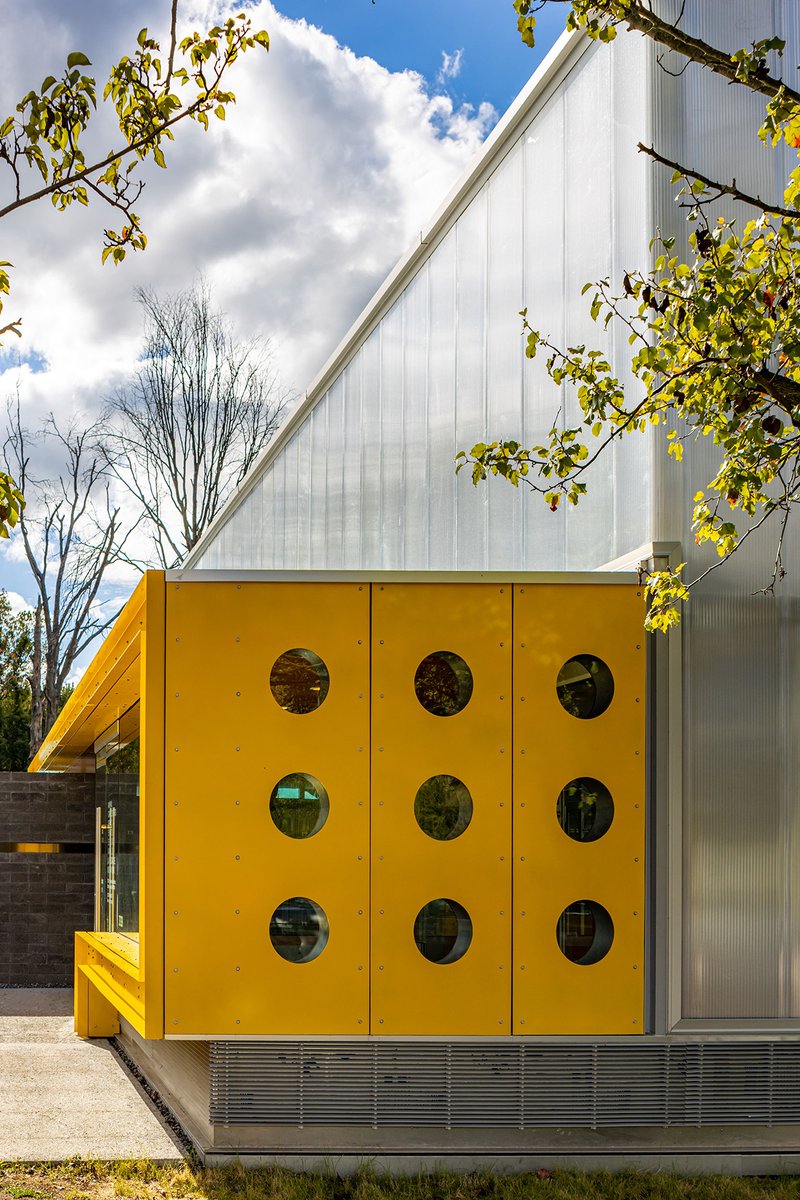 Yellow facade with nine circular porthole windows beneath sloped translucent polycarbonate wall