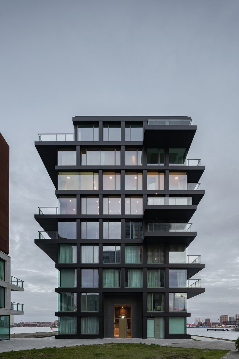 Tower facade with staggered black balconies and floor-to-ceiling glazing photographed at dusk