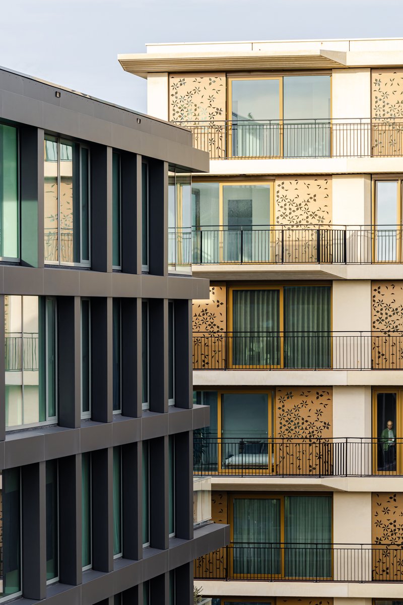 Two residential facades meeting at a corner with vertical metal fins and perforated timber panels over balconies