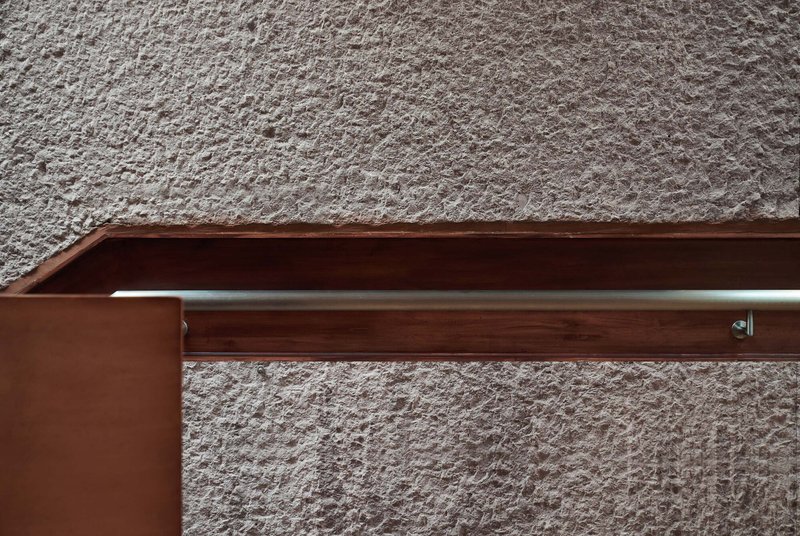 Timber handrail detail with steel rod support against a textured plaster wall