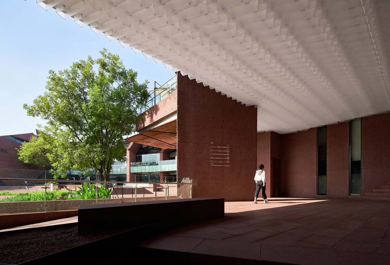 Shaded terrace with coffered ceiling looking out to a tree-lined courtyard and planted water feature