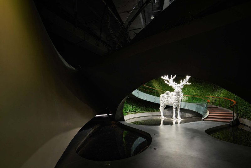 Interior view showing illuminated deer sculpture beside moss-covered walls and organic floor opening