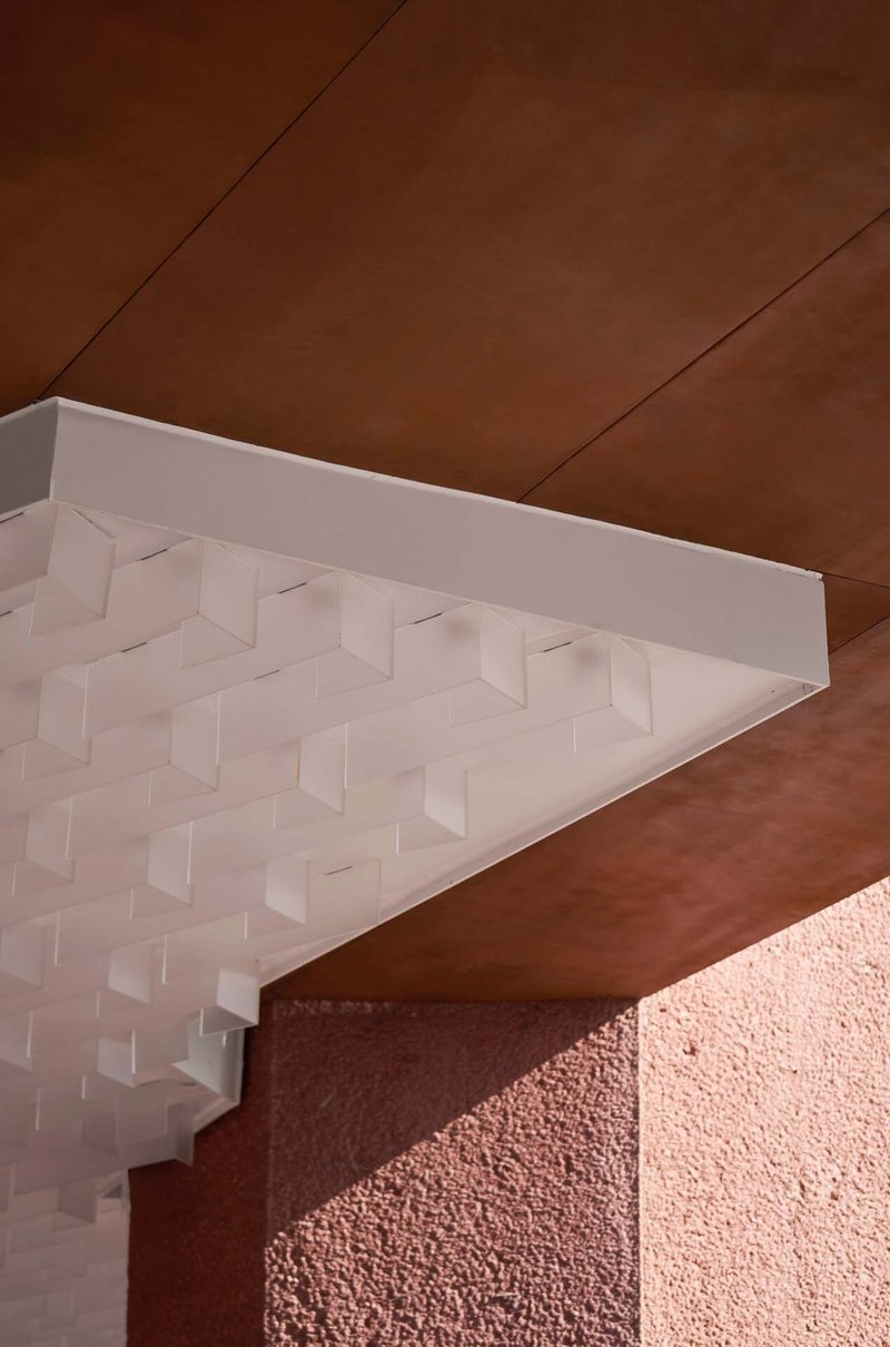 Detail of white three-dimensional coffered ceiling panel meeting a corten steel soffit and pink textured wall