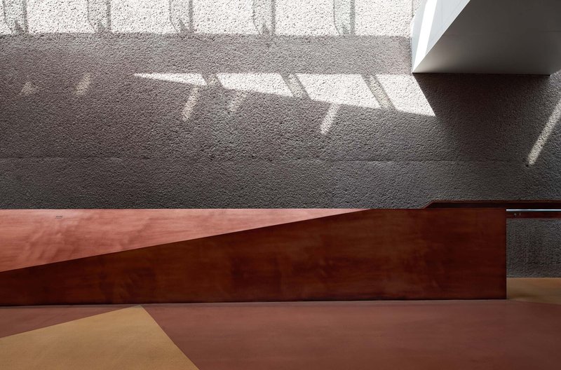 Intersection of corten steel plane and pink floor with patterned shadows from overhead screening