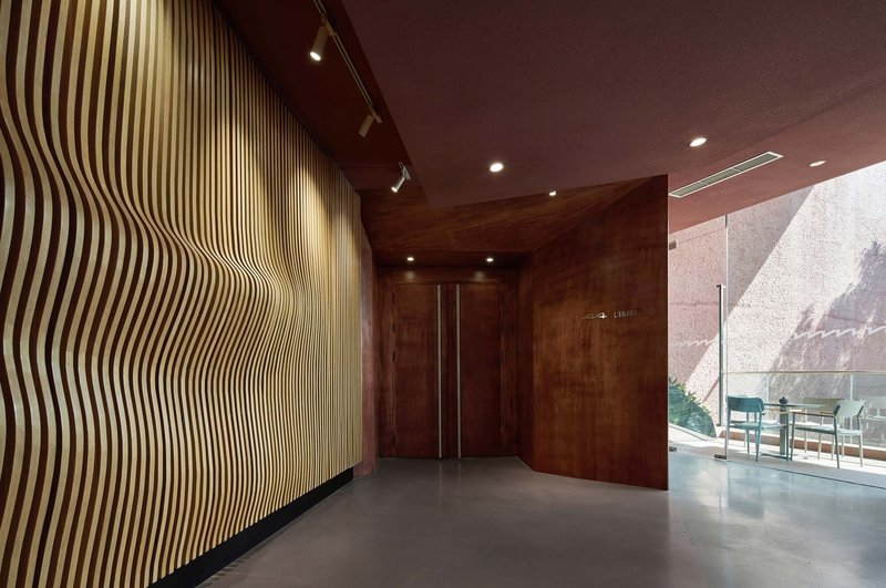 Entrance lobby with undulating wood slat wall and corten steel ceiling under track lighting