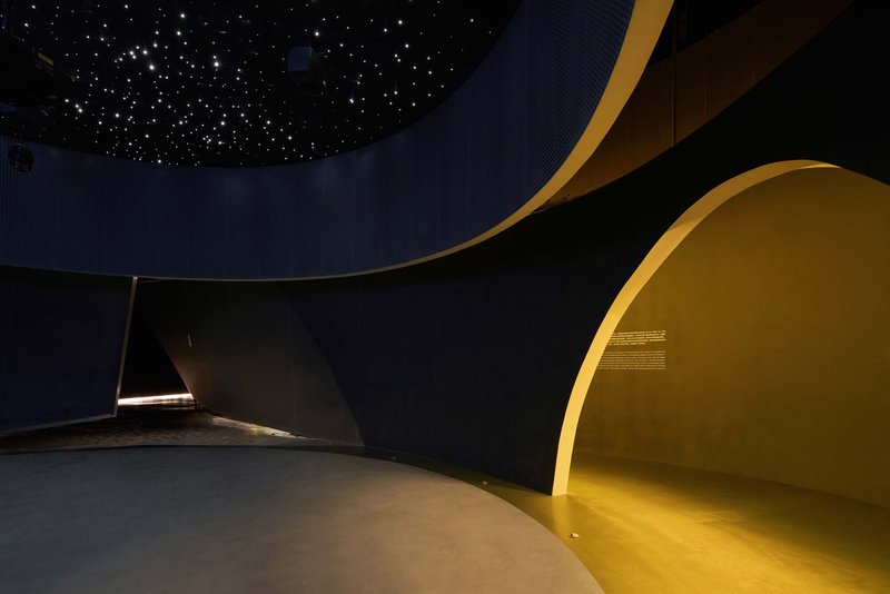 Curved interior wall with yellow illuminated alcove beneath a starlit ceiling