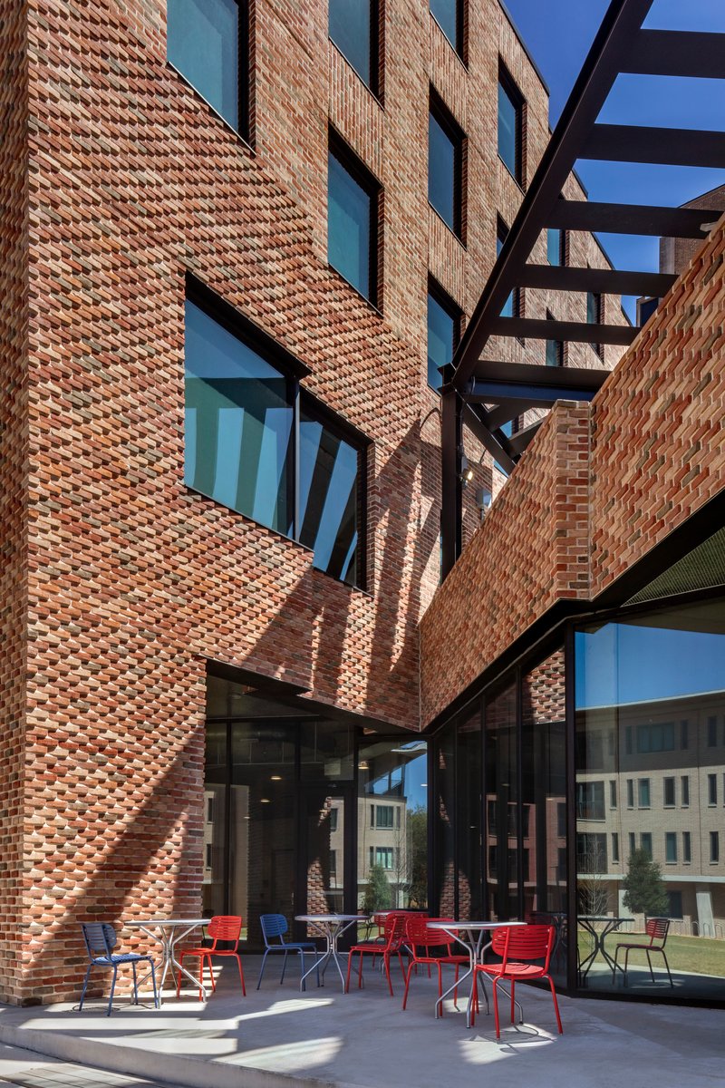 Courtyard looking up at textured brick walls with steel bridge element crossing overhead in late afternoon light