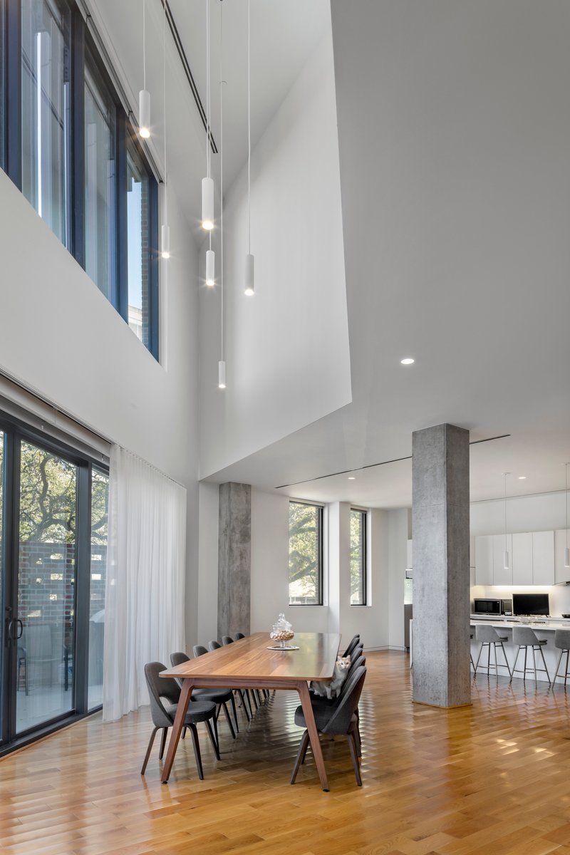 Double-height dining area with concrete columns, wood flooring, and pendant lights descending from the upper level