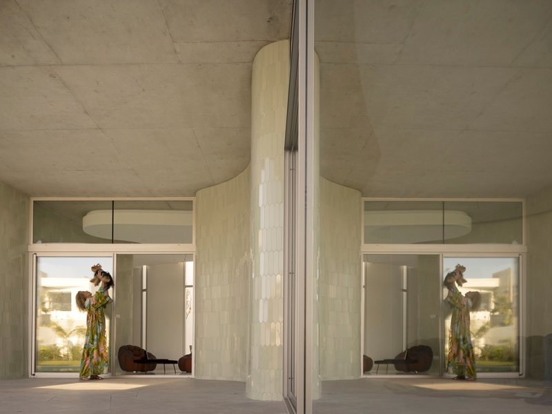 Glass wall reflection showing a person in the interior with exposed concrete ceiling