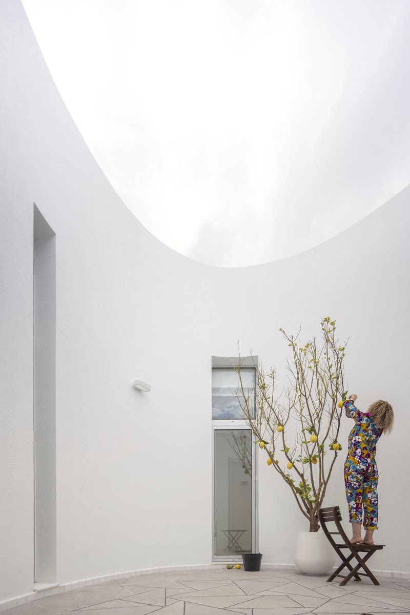 White-walled courtyard with a circular oculus overhead and a person tending to a potted tree