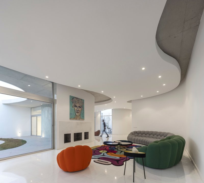 Living room with undulating ceiling cutouts revealing concrete above and colorful furniture below