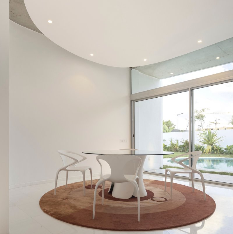 Dining area with circular table on a round rug overlooking a pool and planted courtyard