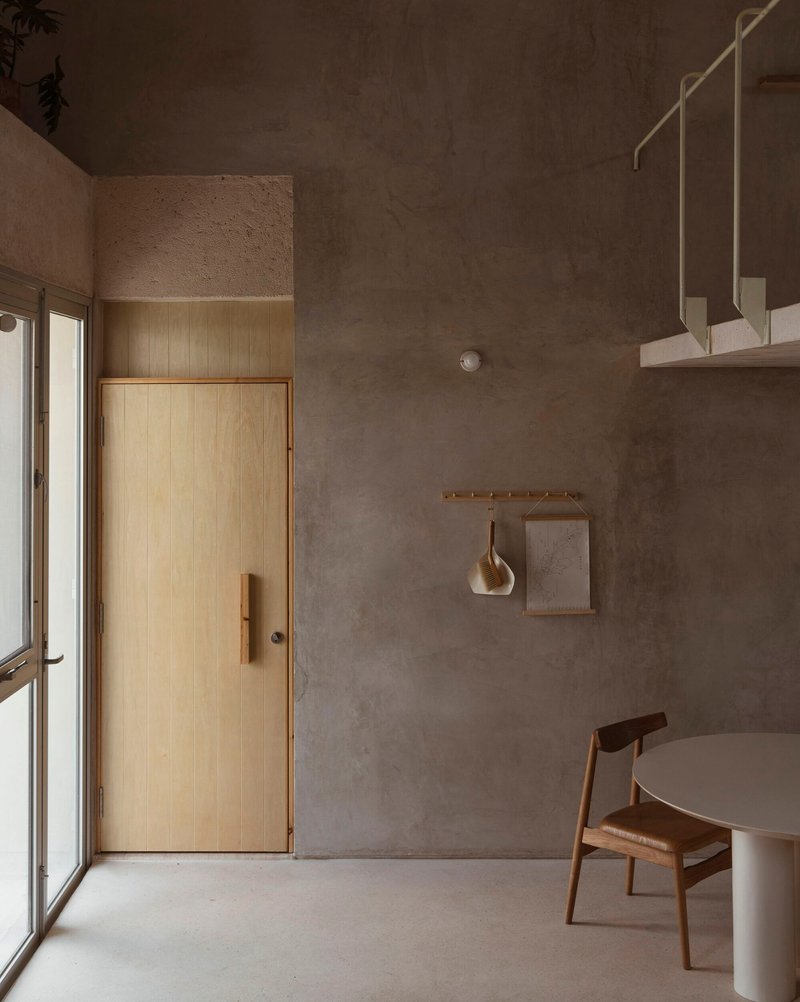 Interior room with raw concrete walls, timber door, suspended brass fixtures and polished concrete floor in soft light