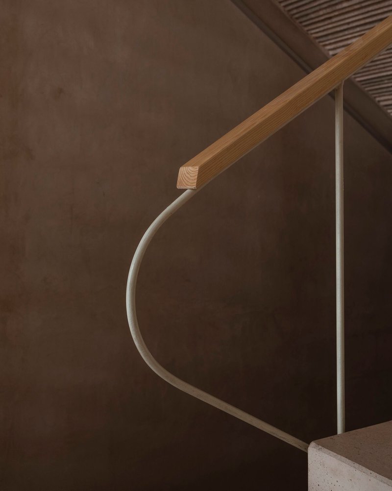 Close-up of curved timber handrail meeting a white metal railing against a concrete wall
