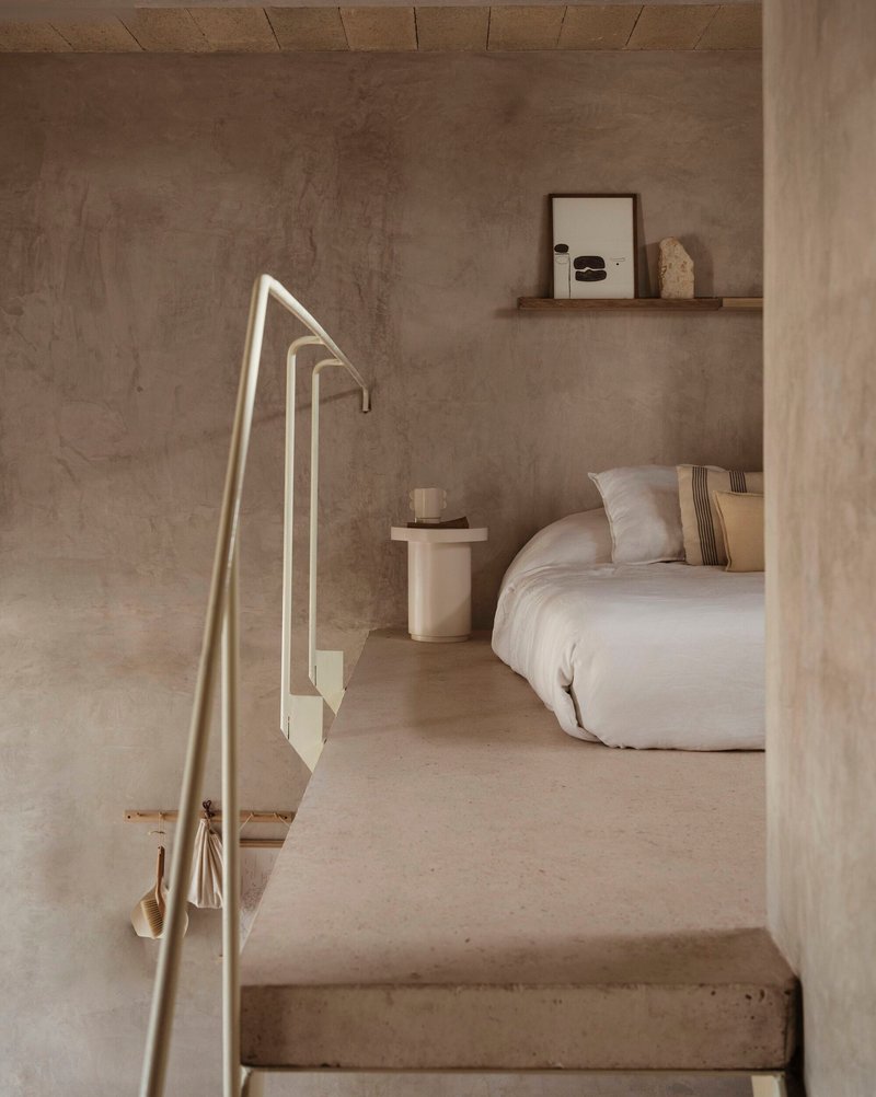 Bedroom entry framed by concrete columns and metal handrail with soft natural light