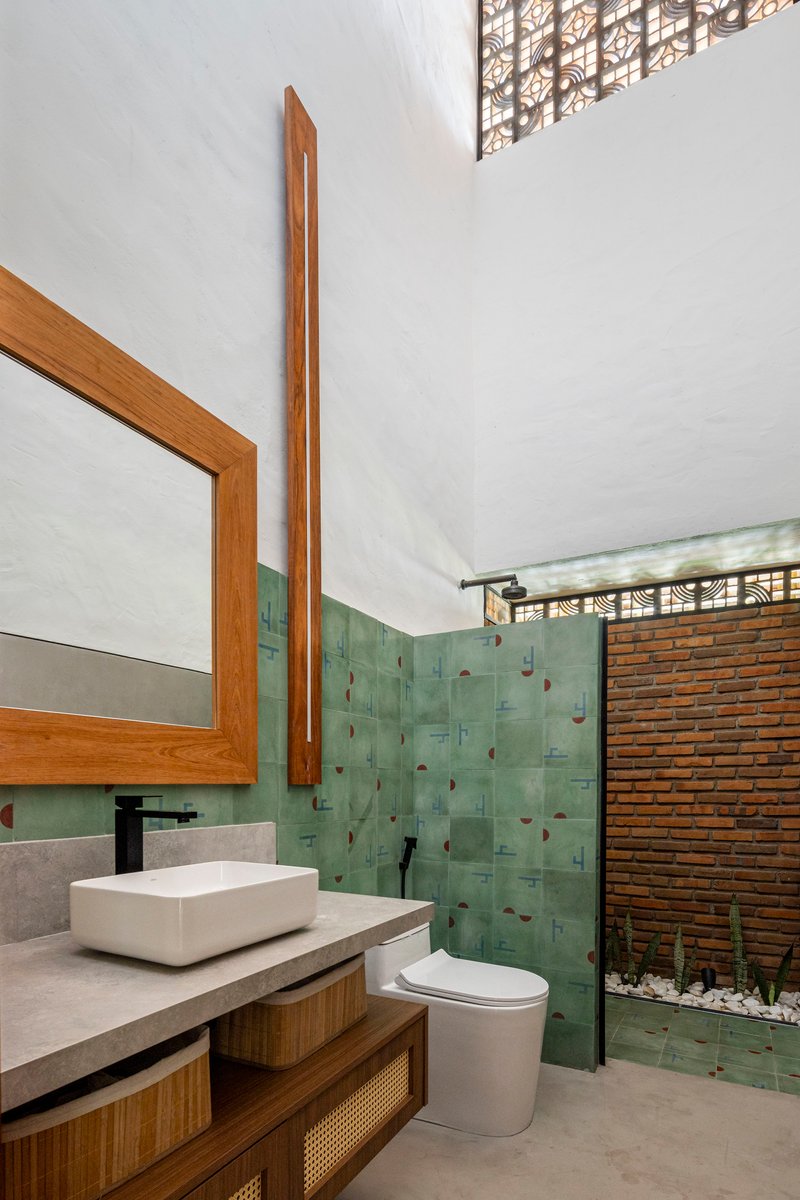 Bathroom with green tile accent wall, timber-framed mirror, and glass shower screen opening to courtyard