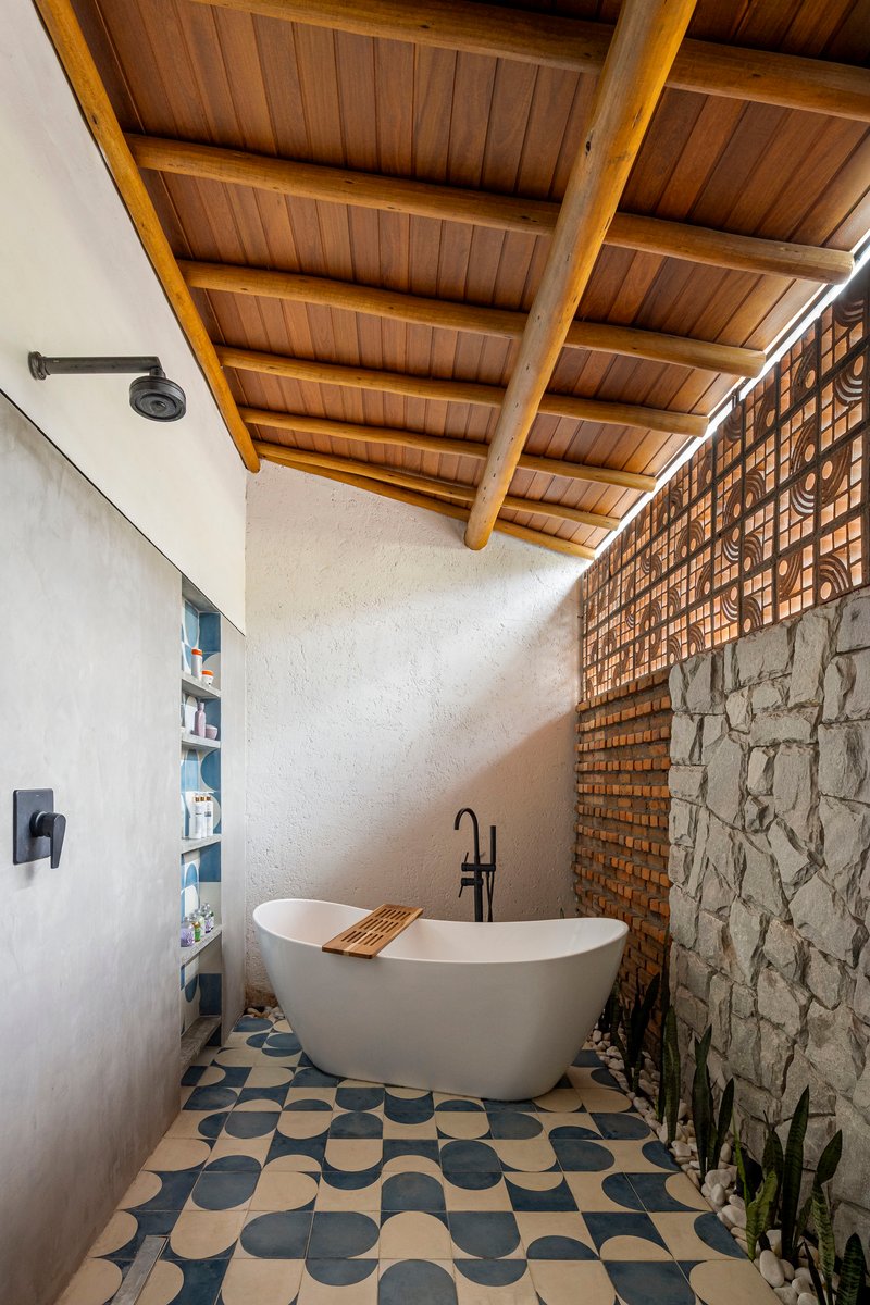 Freestanding bathtub on geometric patterned tile floor beneath timber ceiling with exposed beams and lattice wall