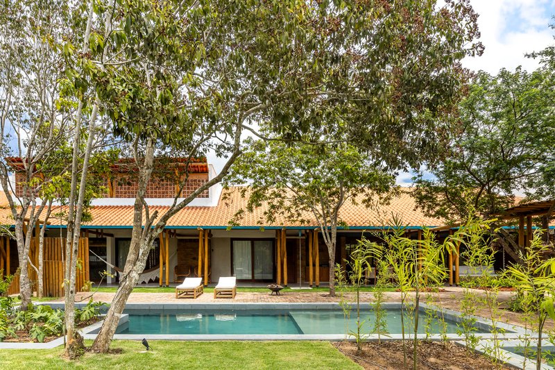 Rear facade with timber columns and tile roof overlooking a swimming pool framed by mature trees