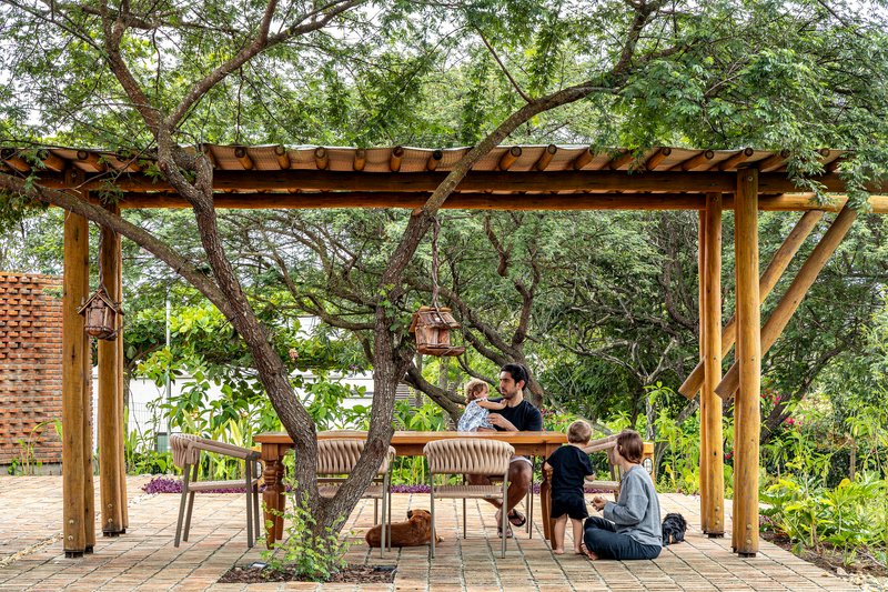 Timber pergola with exposed rafters sheltering a dining table and benches beneath mature trees