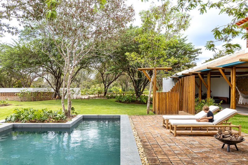 Pool terrace with brick pavers and wooden loungers beside a vertical timber screen and lawn