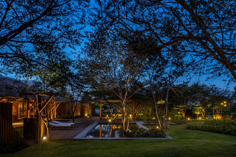Garden courtyard with rectangular reflecting pool surrounded by timber pavilions and uplighted trees at twilight