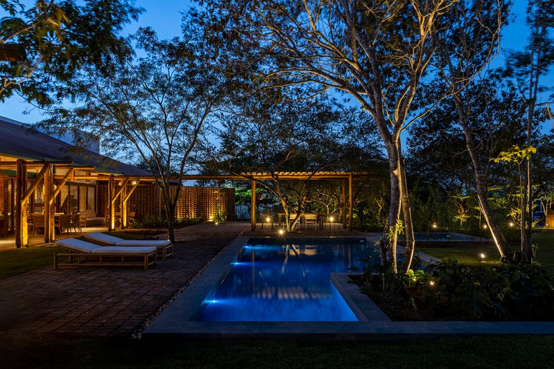 Pool terrace with timber deck and loungers framed by mature trees and uplighting at blue hour