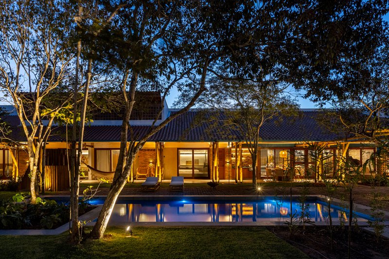 Tiled roof pavilion with glass doors opening to pool courtyard beneath canopy of trees at evening