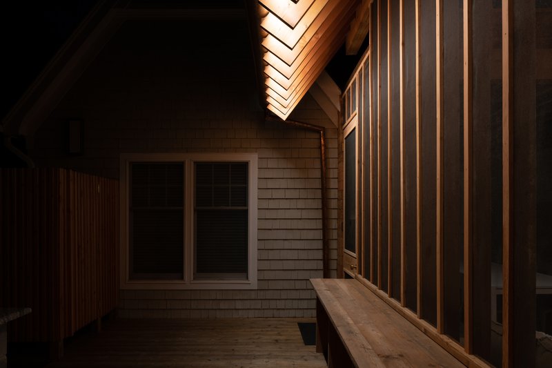 Nighttime view of the timber deck with illuminated vertical slat screen and exposed roof rafters