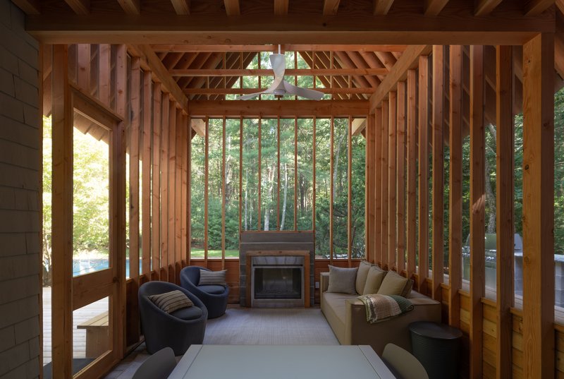 Interior of the timber frame pavilion showing exposed rafters, vertical slats and fireplace with forest view