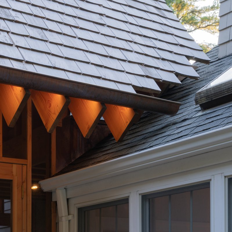Junction of slate shingle roofs with exposed timber eaves and triangular soffit openings at dusk
