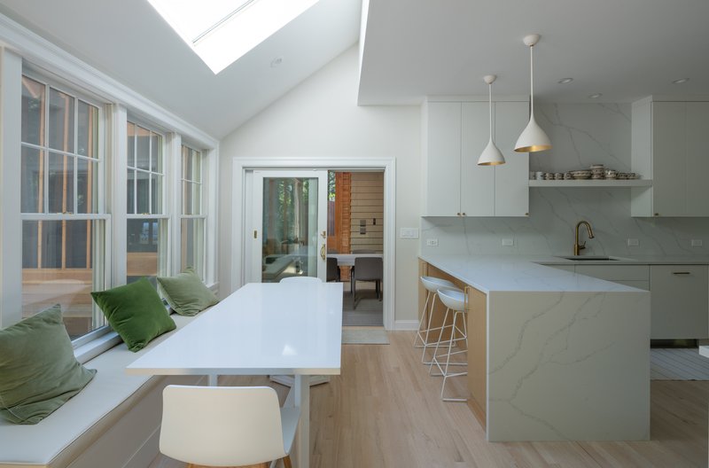 White kitchen with island and pendant lights adjacent to a window seat flooded with daylight